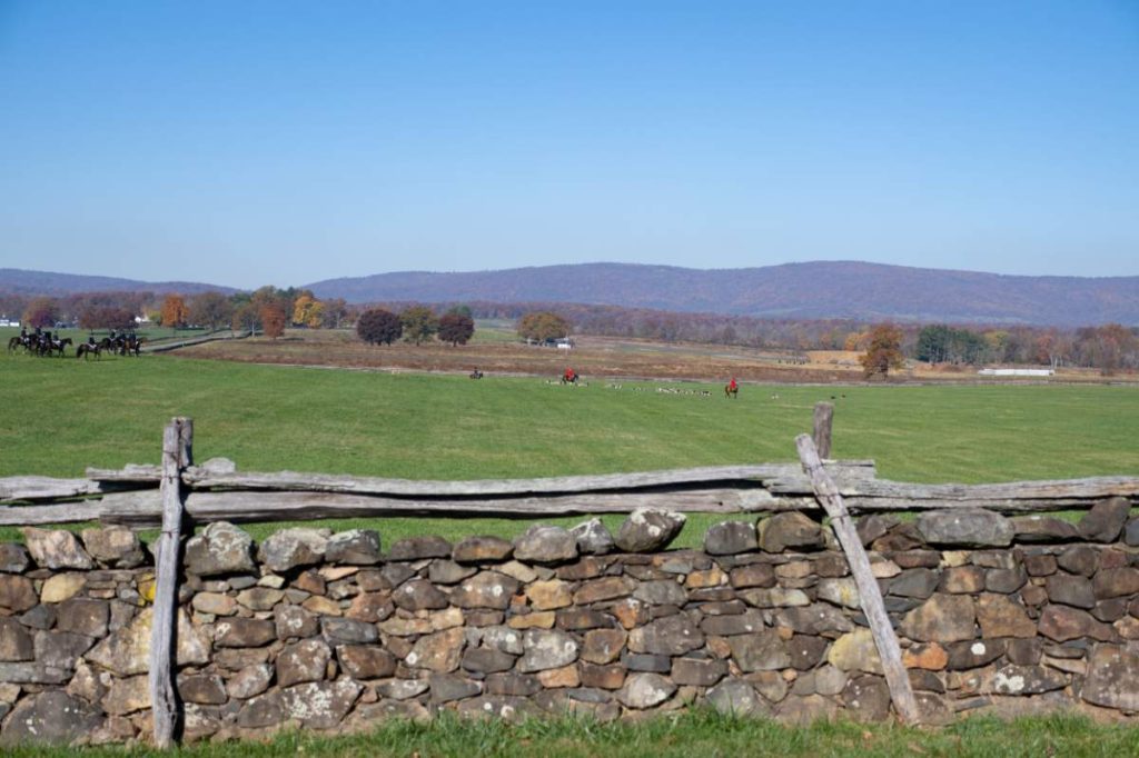 virginia countryside with stone wall in foreground, foxhunters coming across field