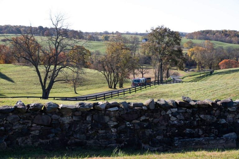 fire truck going up road between pasture and stonewall in foreground