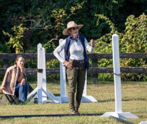 instructor standing in horse riding ring by jump standards